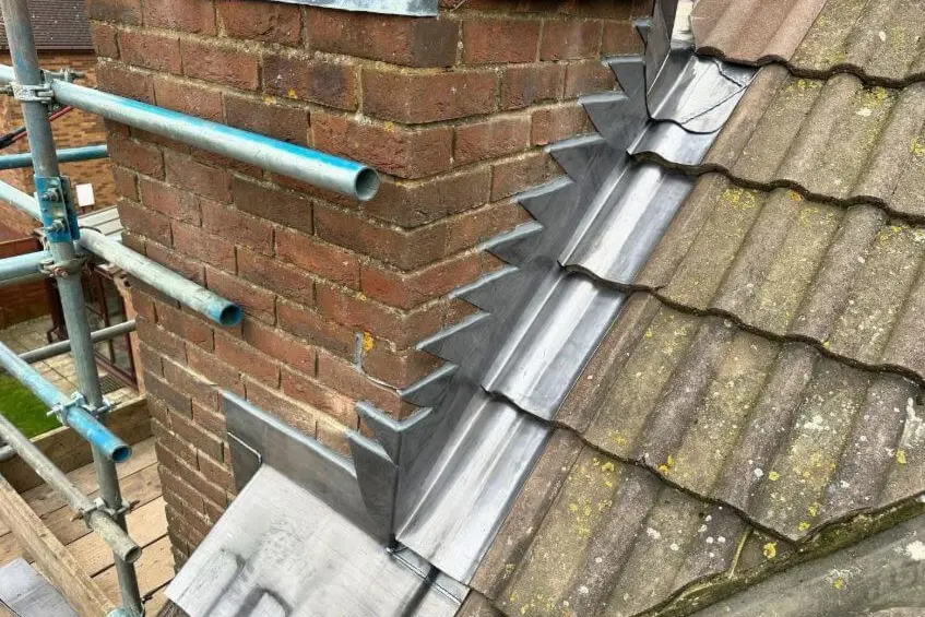 A brick chimney stack being repointed above a tiled roof