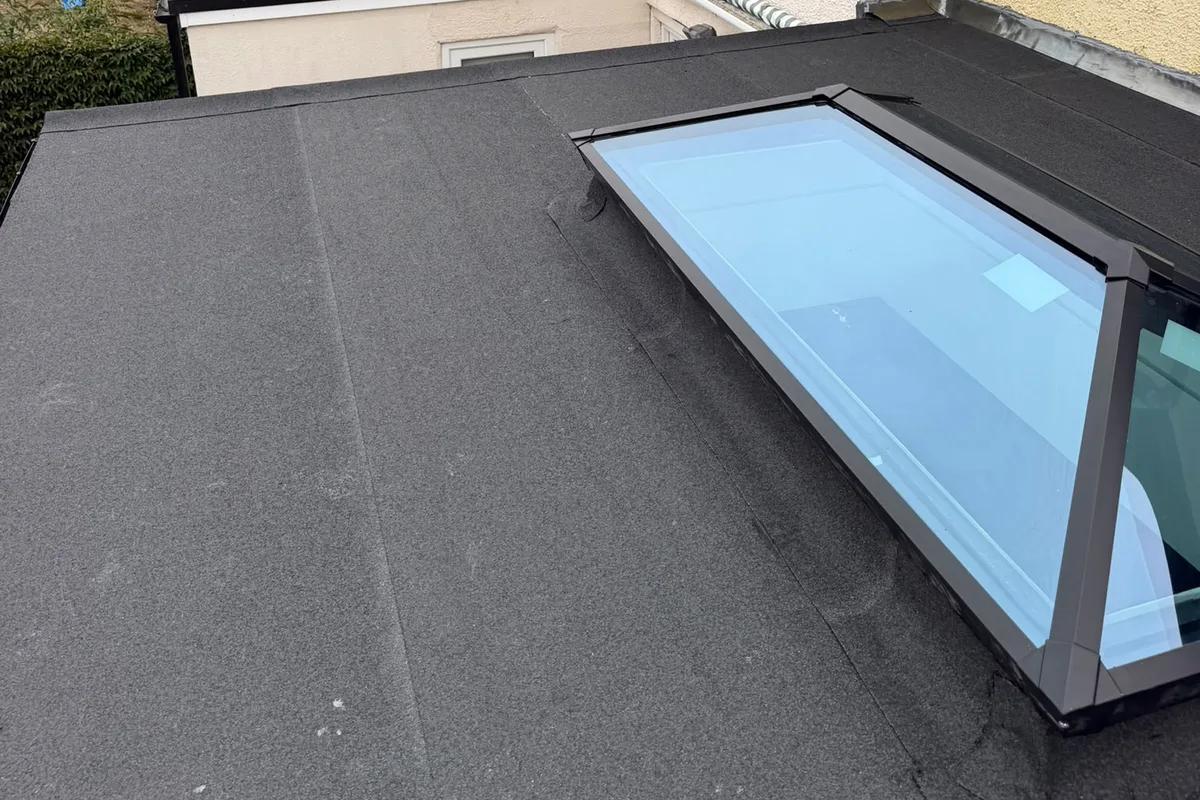 A torch-on felt flat roof running up to a glass lantern, with the house behind