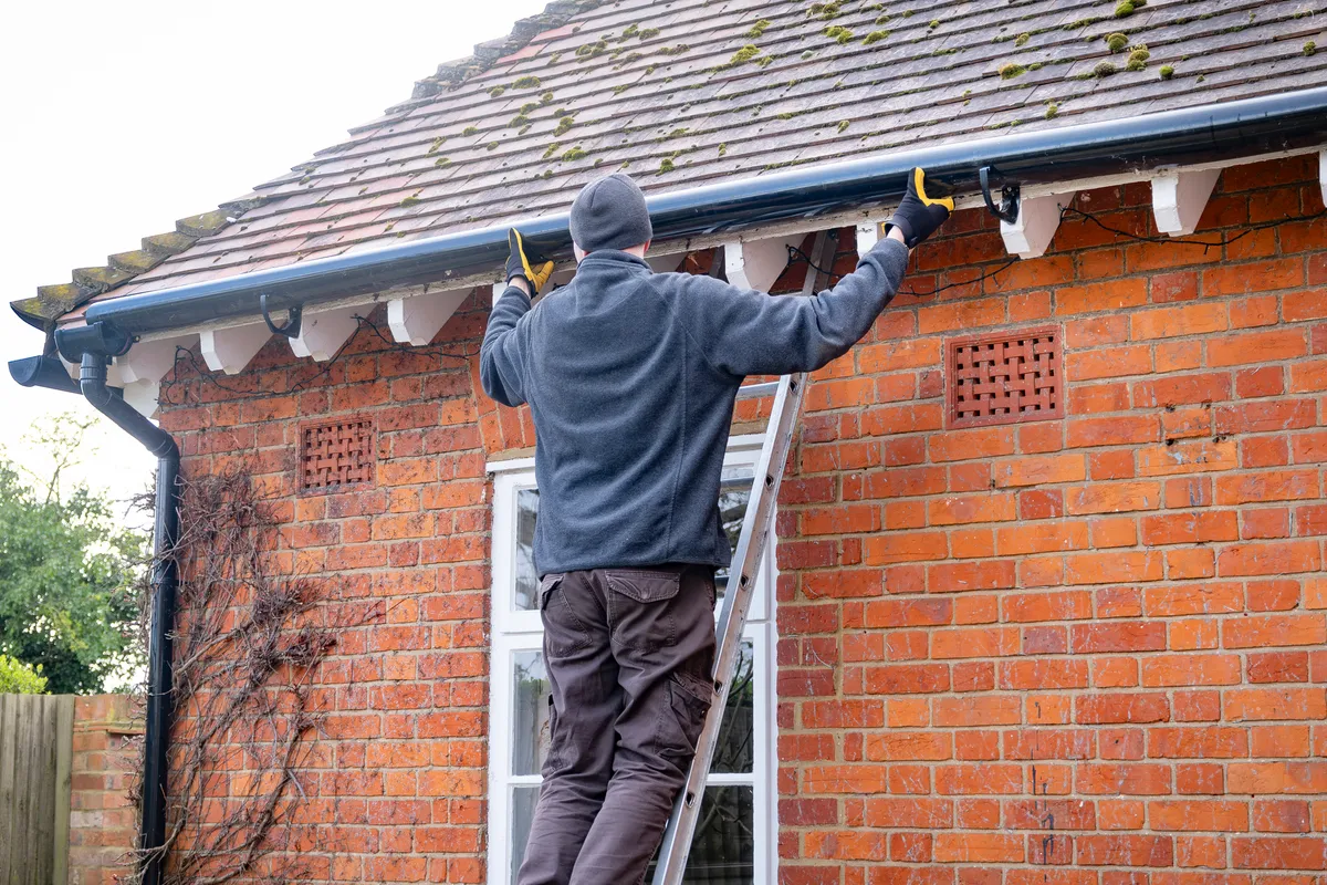 A gutter being cleared and refitted from a ladder