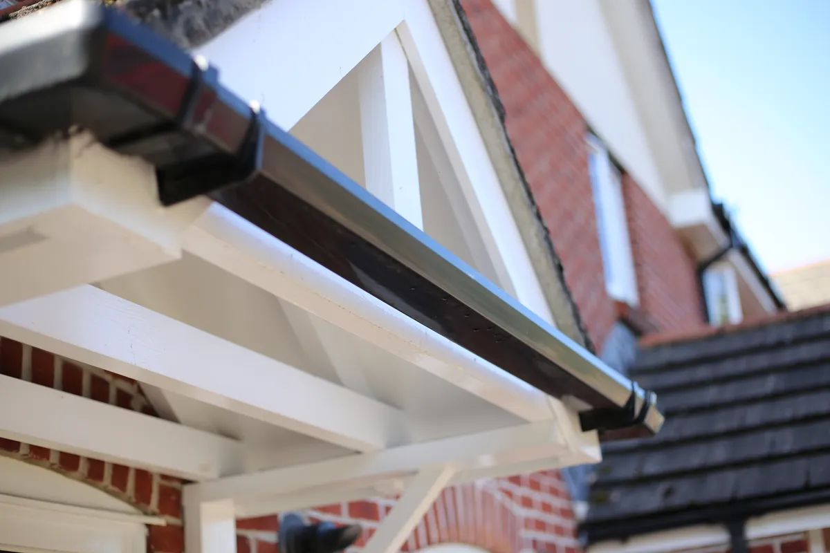 A black gutter and downpipe on a white porch canopy over red brick