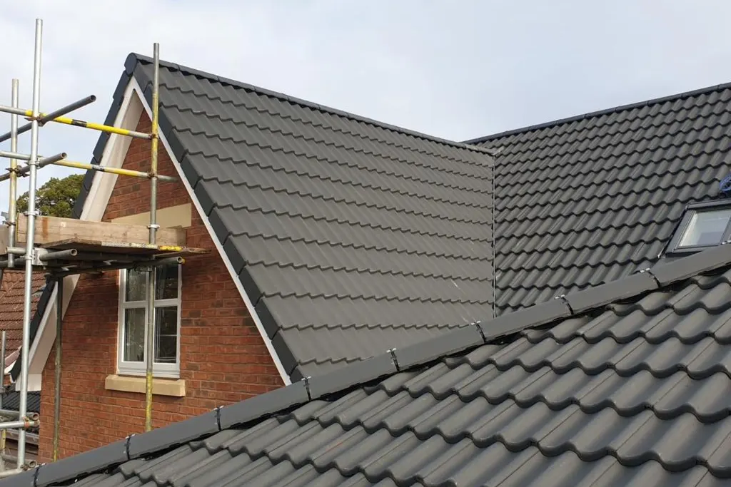 A new dark tiled roof and dormer on a brick house, scaffold still up