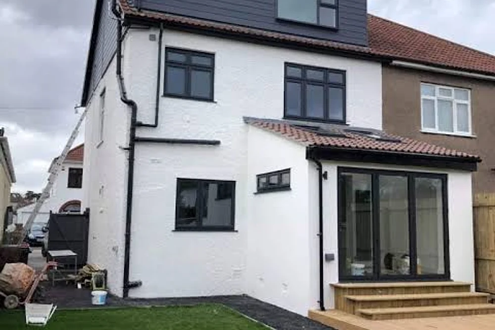 A white rendered house with a dark dormer and a new rear extension