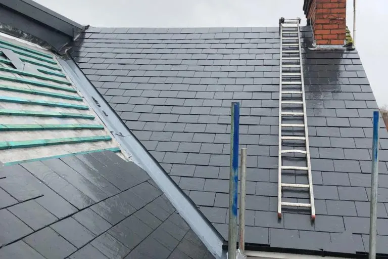 Repair work in progress on a slate roof, ladder and lead valley in view